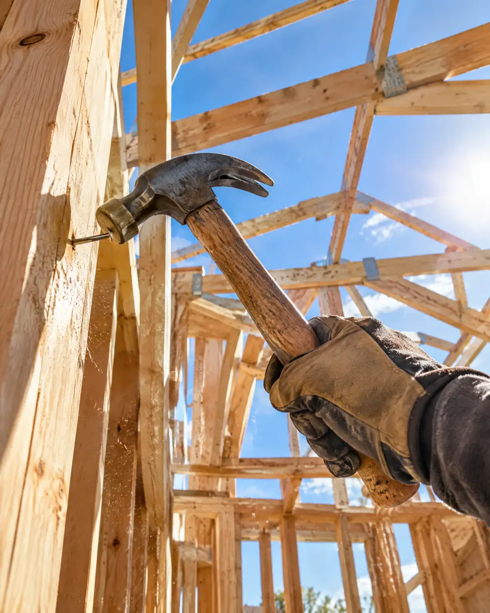 Looking up through new wood framing at blue sky as a carpenter drives a nail