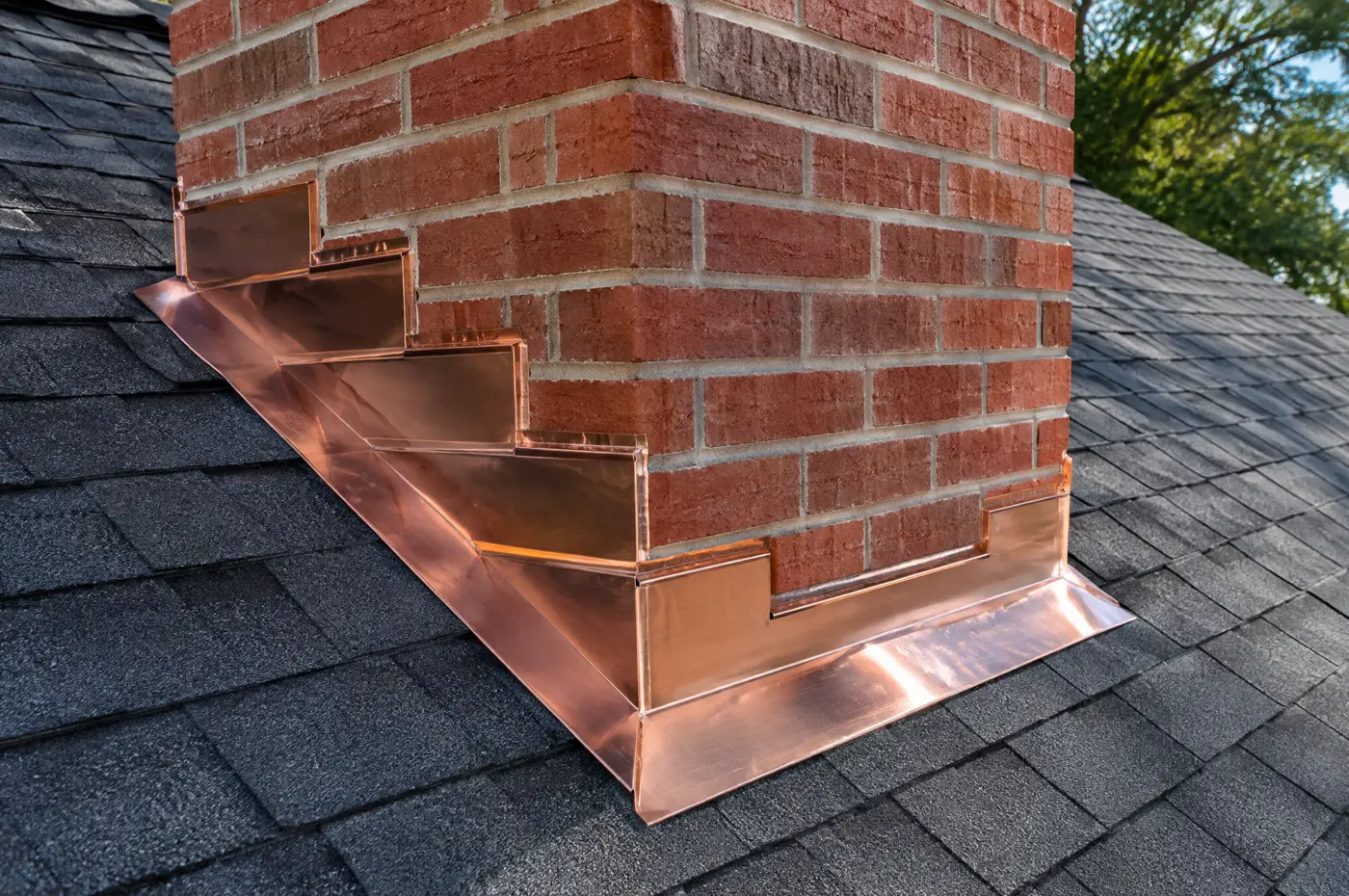 New copper flashing tucked into the mortar of a brick chimney
